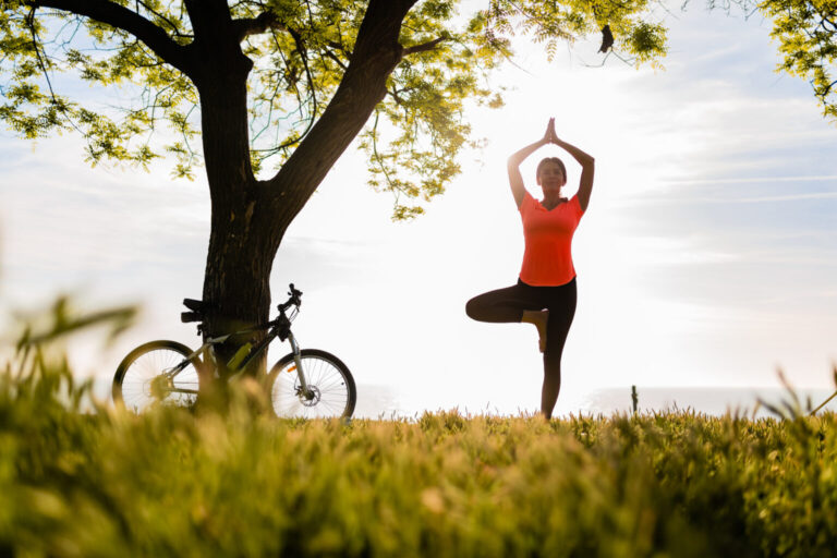 slim beautiful woman silhouette doing sports in morning in park doing yoga on mat in colorful fitness outfit in nature, smiling happy healthy lifestyle, calm meditation, bicycle on background